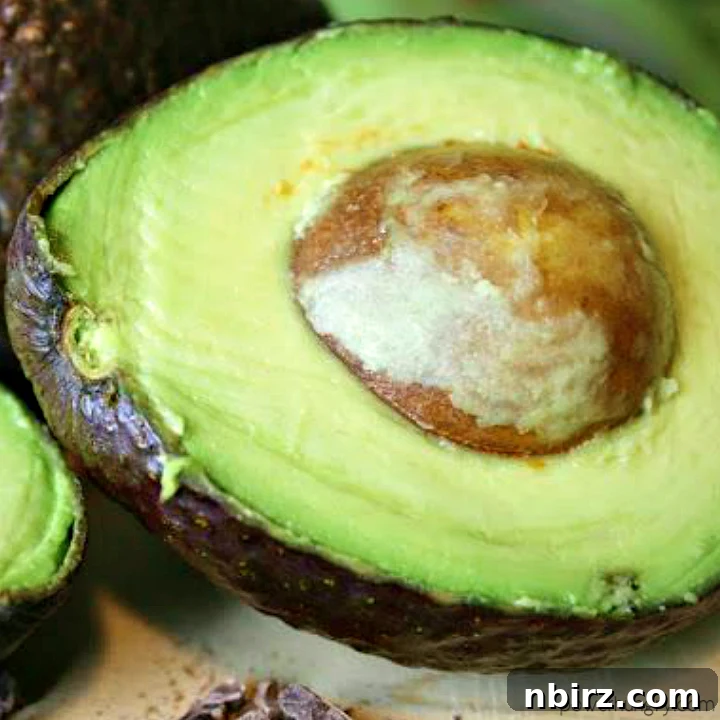 Close up of a halved avocado on a wooden cutting board, revealing its creamy green flesh and pit.