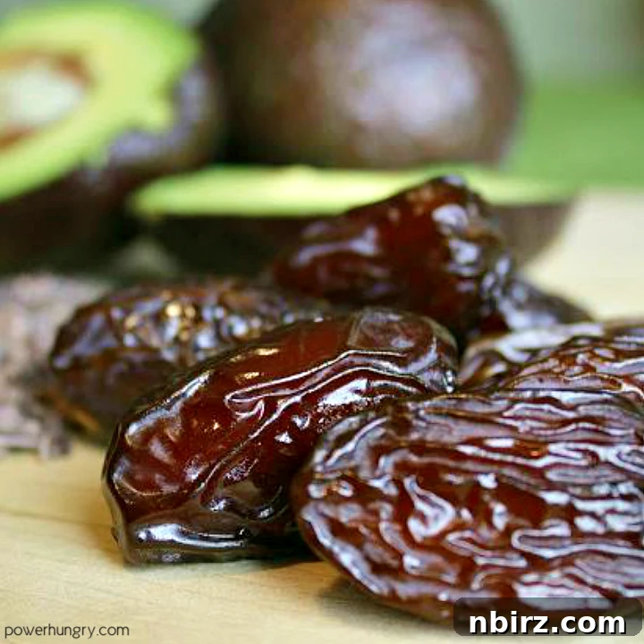 A selection of pitted Medjool dates and a whole avocado on a wooden cutting board, ready for pudding preparation.