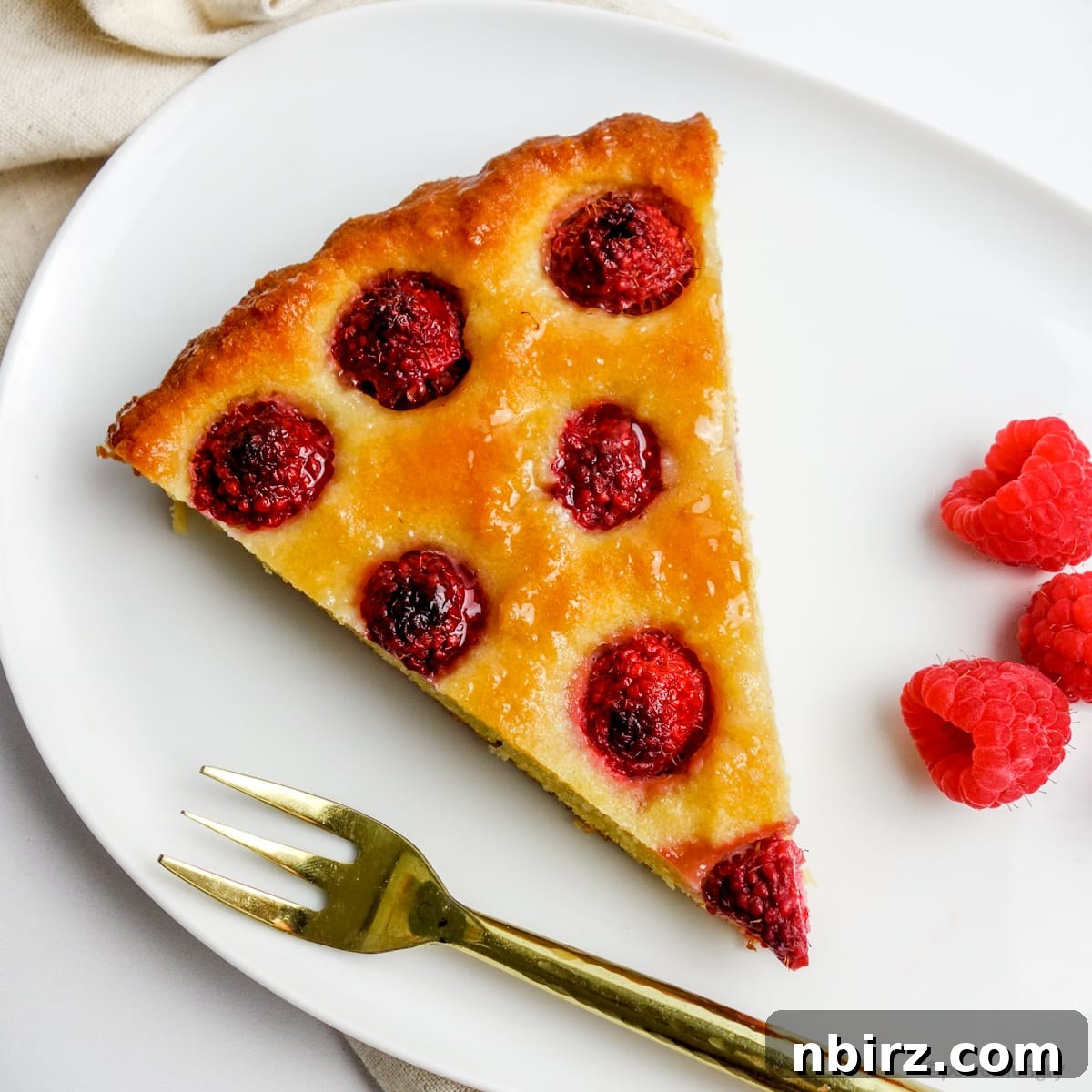 Vegan Raspberry Tart: A Gluten-Free Delight 3 A slice of vegan no-crust raspberry almond tart on a white plate with fresh raspberries