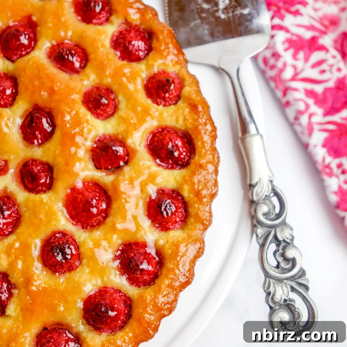Vegan Raspberry Tart: A Gluten-Free Delight 9 Close up of the side of a glazed vegan no-crust raspberry almond tart on a white cake stand