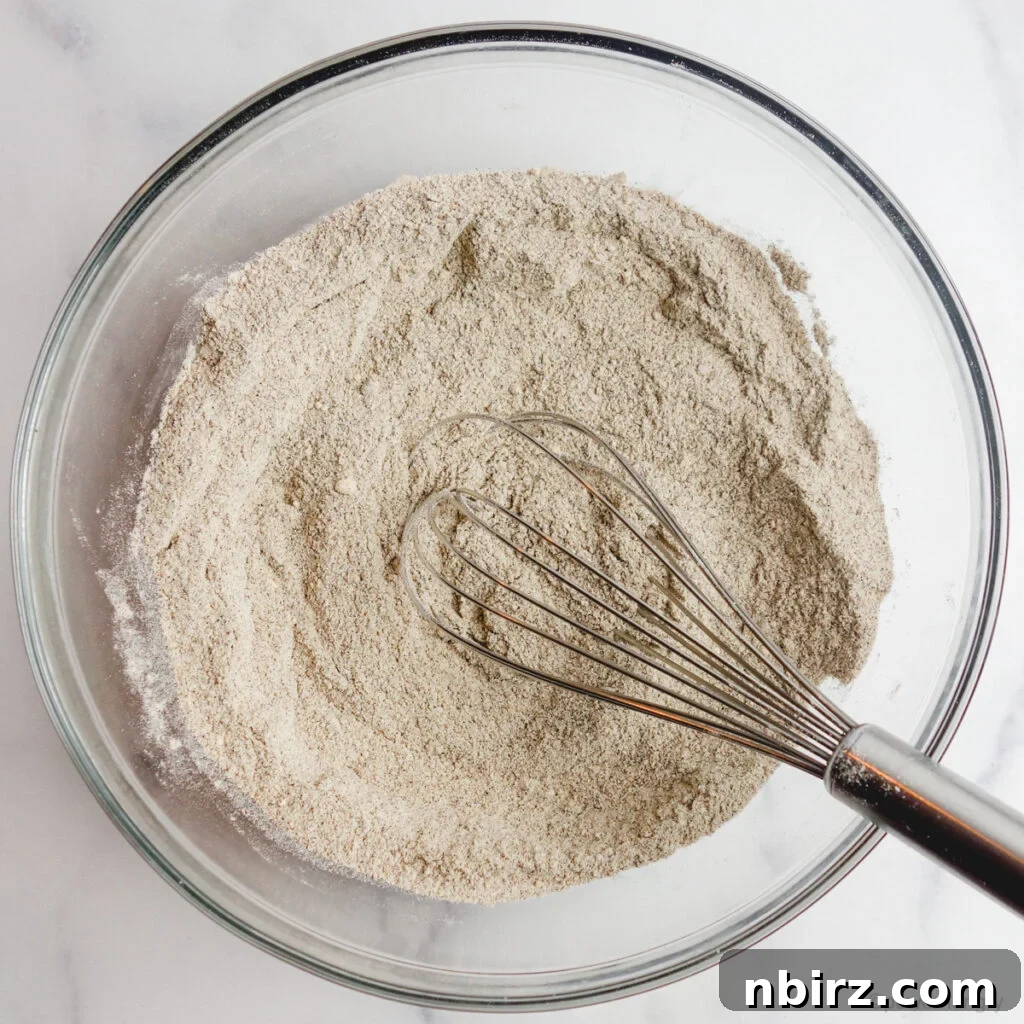 The dry ingredients for buckwheat flour muffins, including flours, sugar, and leavening agents, thoroughly whisked together in a clear glass bowl.