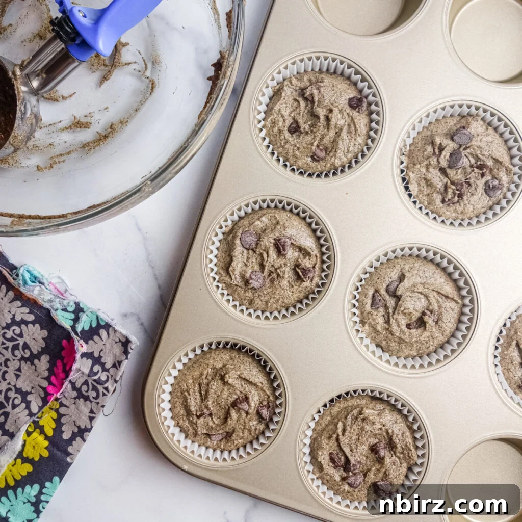 Buckwheat flour muffin batter neatly portioned into white paper-lined muffin cups, filling them almost to the brim.