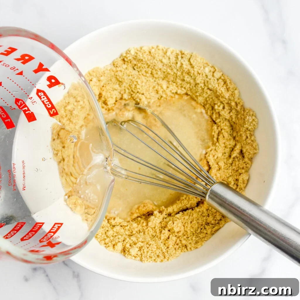 One-Bowl Vegan Flax Waffles (Keto, Gluten-Free Option) 7 Water being poured from a glass measuring cup into a white bowl filled with flaxseed meal, starting the batter
