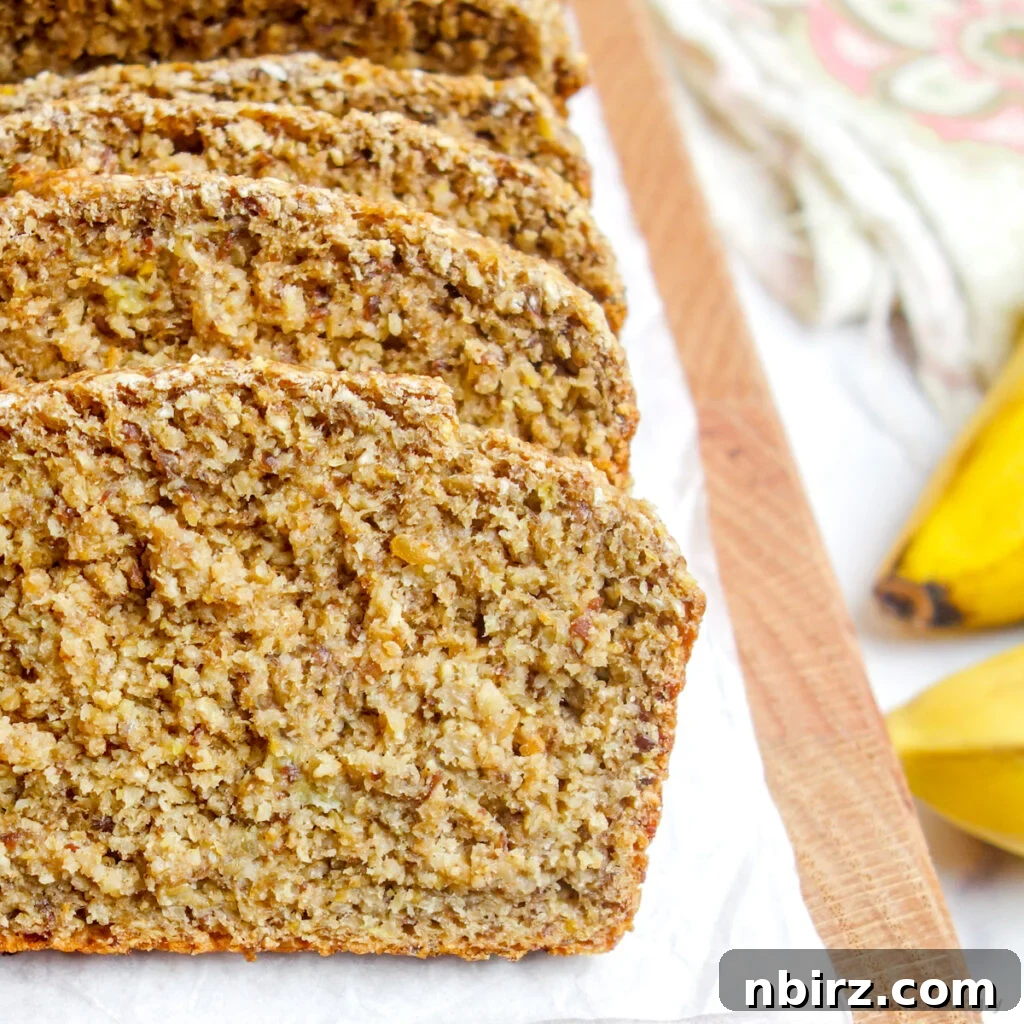 Close up of perfectly sliced vegan oat flour banana bread on a wooden cutting board, highlighting its moist texture.