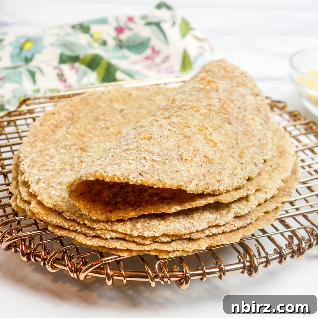 A neat stack of golden millet flax tortillas arranged on a copper cooling rack, one tortilla gently folded in half, showcasing its soft pliability.