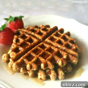 Golden brown vegan almond flour waffles on a white plate, garnished with fresh strawberries and drizzled with maple syrup.