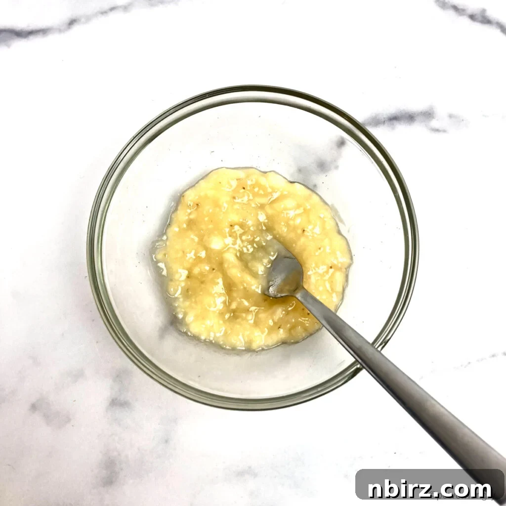 Effortless Two-Ingredient Vegan Gluten-Free Oil-Free Peanut Butter Banana Cookies 5 finely mashed banana in a glass bowl atop a white marble countertop