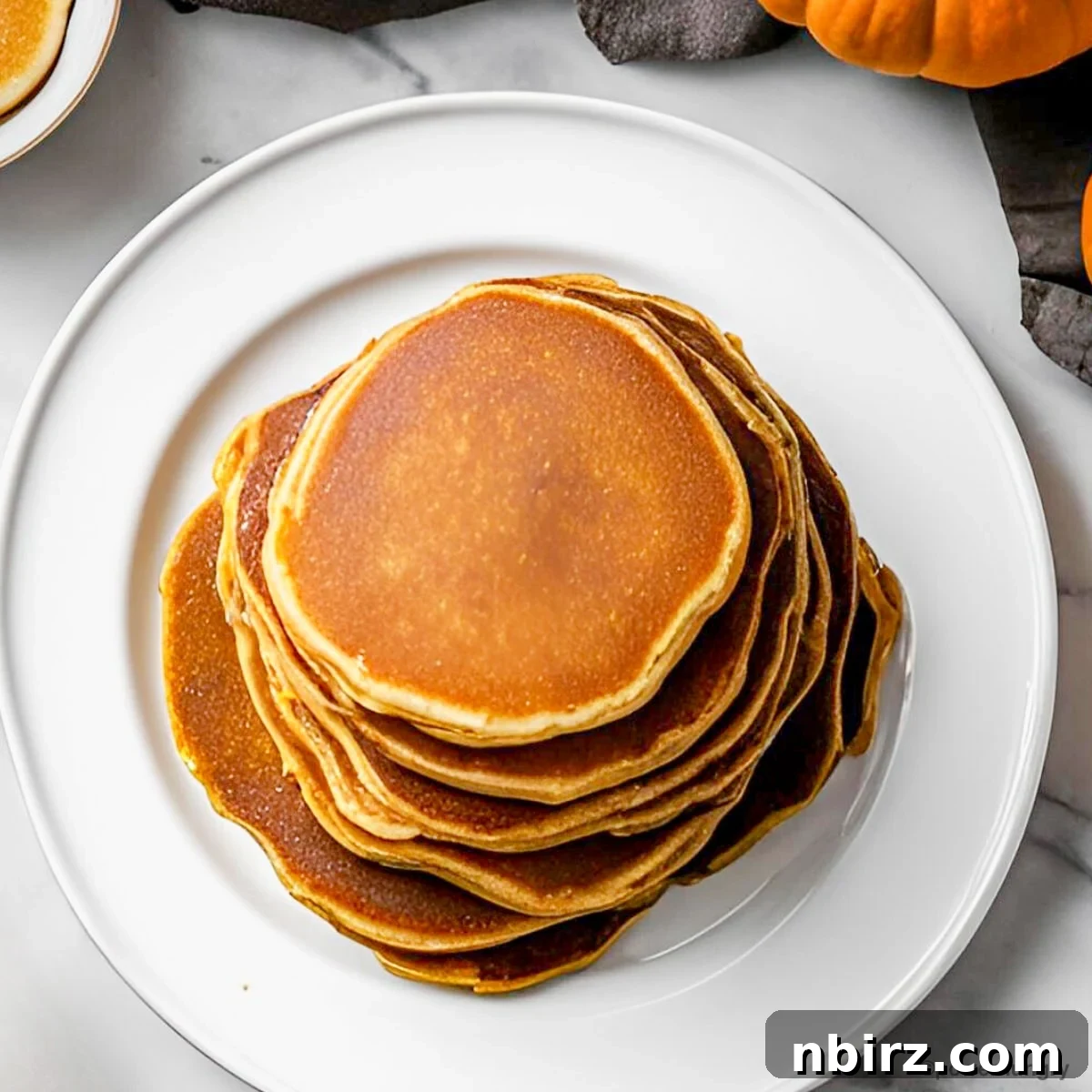 Wholesome Vegan Coconut Flour Pumpkin Pancakes Oil-Free and Grain-Free 3 An inviting overhead shot of a generous stack of warm pumpkin coconut flour pancakes, beautifully arranged, highlighting their fluffy texture and golden-brown edges. Drizzled with a touch of maple syrup and ready for a comforting breakfast.