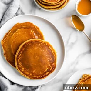 A perfectly cooked stack of coconut flour pumpkin pancakes, ready for serving on a clean white plate.