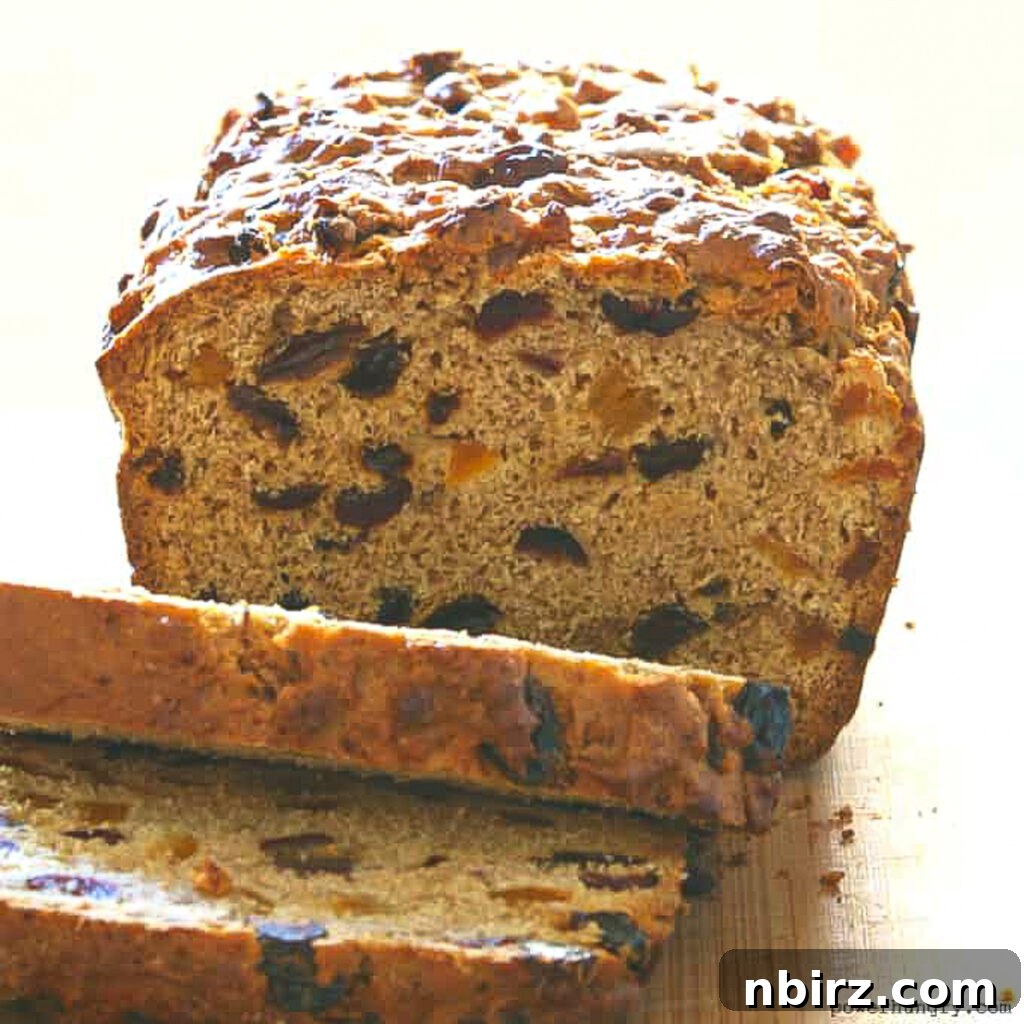 A freshly baked loaf of sliced Bara Brith, a vegan Welsh fruit bread, displayed on a cool blue surface, highlighting its golden crust and fruit-filled interior.