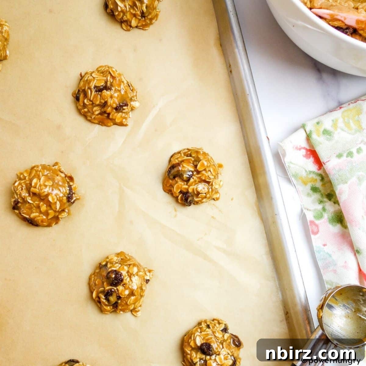 Wholesome Vegan Oatmeal Raisin Cookies No Oil No Gluten 5 Perfectly scooped vegan oatmeal raisin cookie dough portions neatly arranged on a parchment-lined cookie sheet, ready for baking.