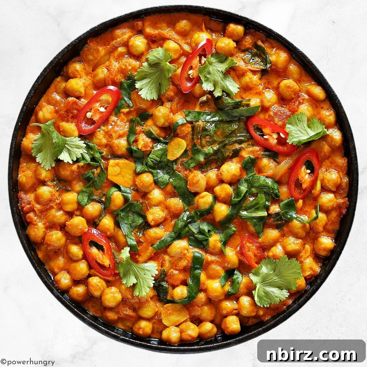 Close-up of a fast chickpea spinach curry in a dark brown bowl, garnished with fresh cilantro.