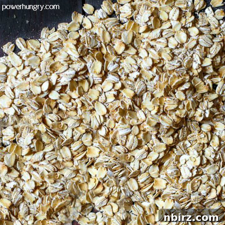 Old-fashioned rolled oats spread out on a black cutting board, showcasing their natural texture