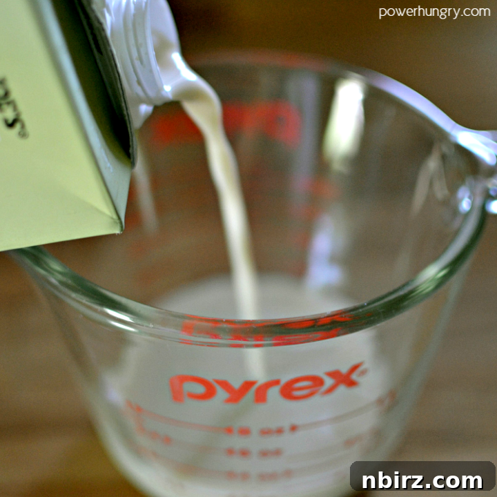 Overhead shot of nondairy milk being poured into a clear glass measuring cup, ready for the recipe
