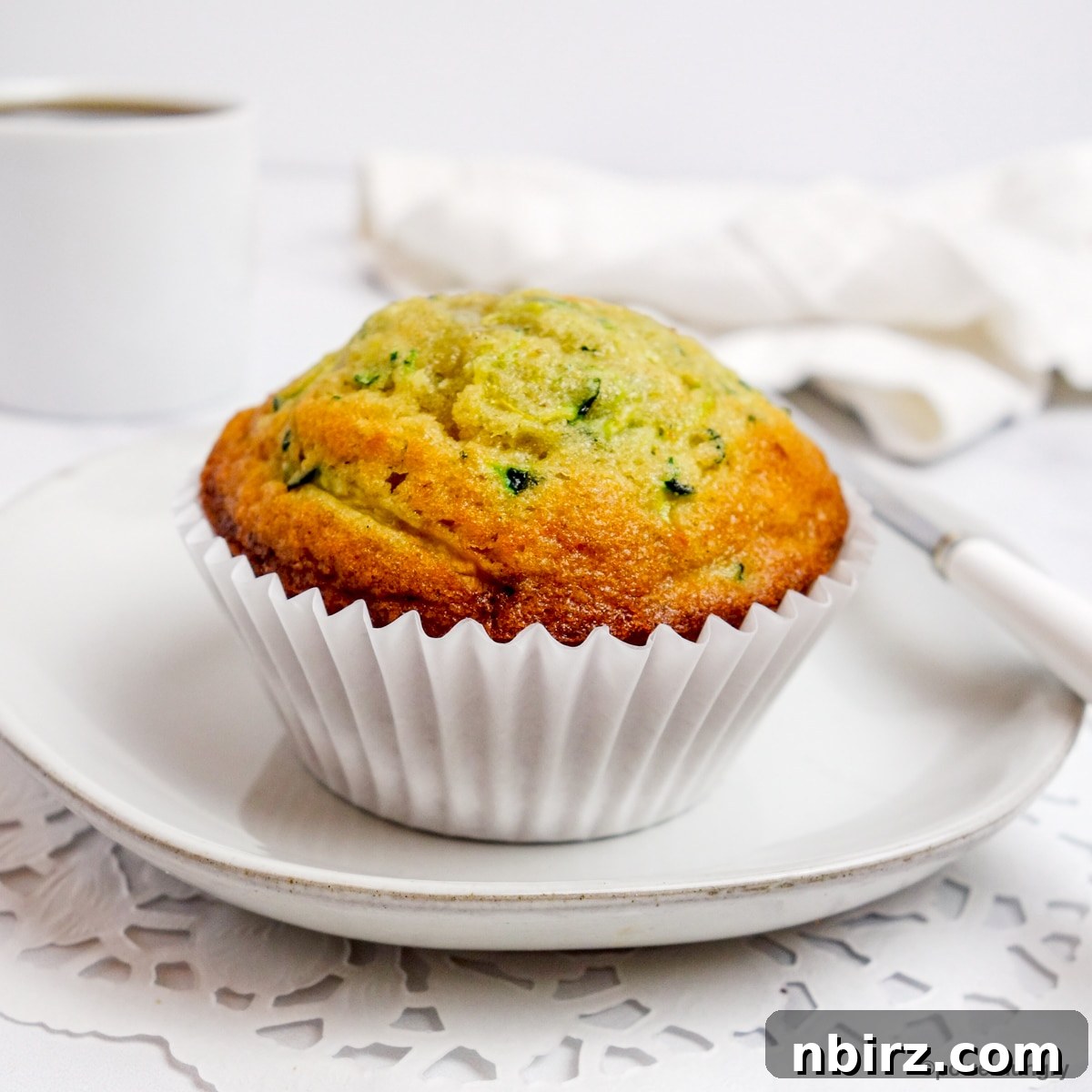 A single 3-ingredient chickpea flour zucchini muffin placed on a pristine white plate, showcasing its golden brown crust.