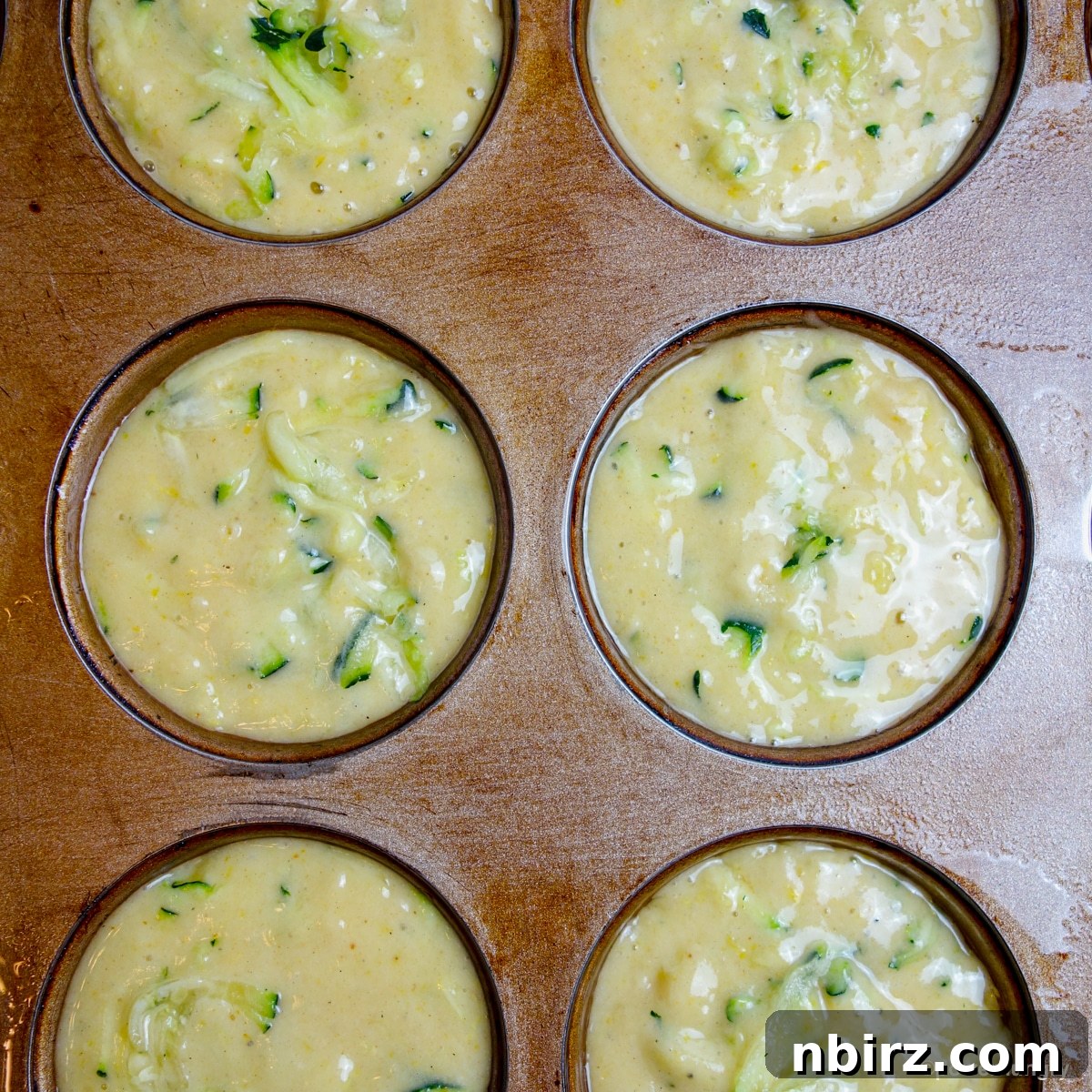 Muffin tin with 3-ingredient vegan zucchini muffin batter neatly portioned into each liner, ready for the oven.