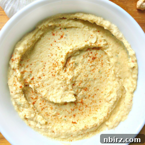 Overhead shot of a white bowl filled with oil-free and tahini-free hummus, sprinkled with smoked paprika and a fresh lemon wedge.