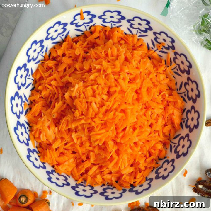 Overhead shot of a blue and white bowl filled with grated carrots and chickpeas, ready to be marinated