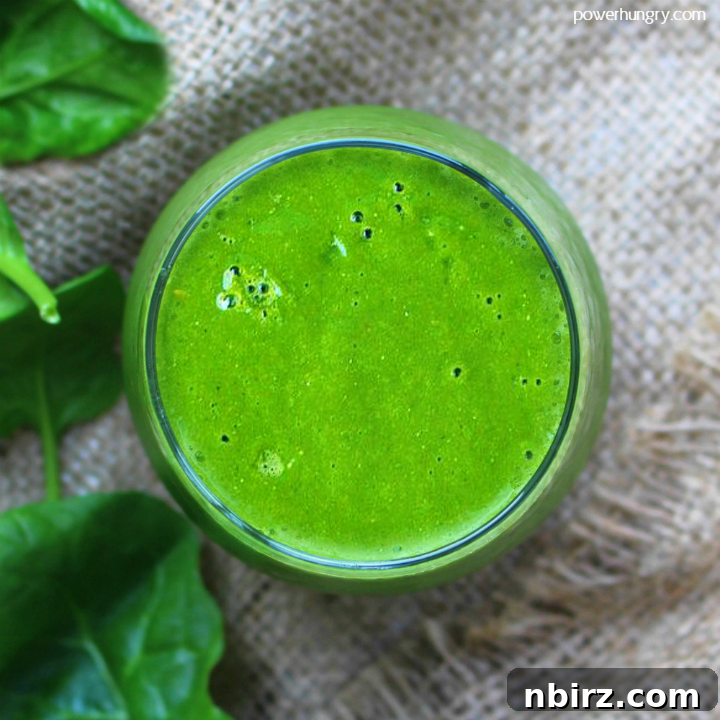 Revitalizing Green Energy Smoothie 2 Vibrant green smoothie in an elegant glass jar, garnished with a slice of lime, set against a rustic background with fresh spinach leaves and half an avocado.