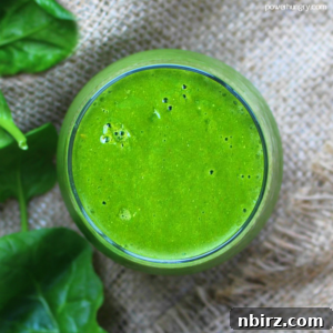 Revitalizing Green Energy Smoothie 4 A tall glass jar filled with the vibrant green energy renewal smoothie, garnished with a fresh lime wedge and a straw, presented on a rustic burlap surface.