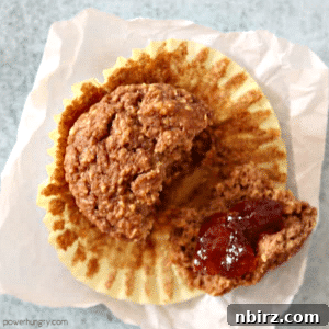 vegan oat bran muffin on a piece of parchment paper, one piece spread with jam