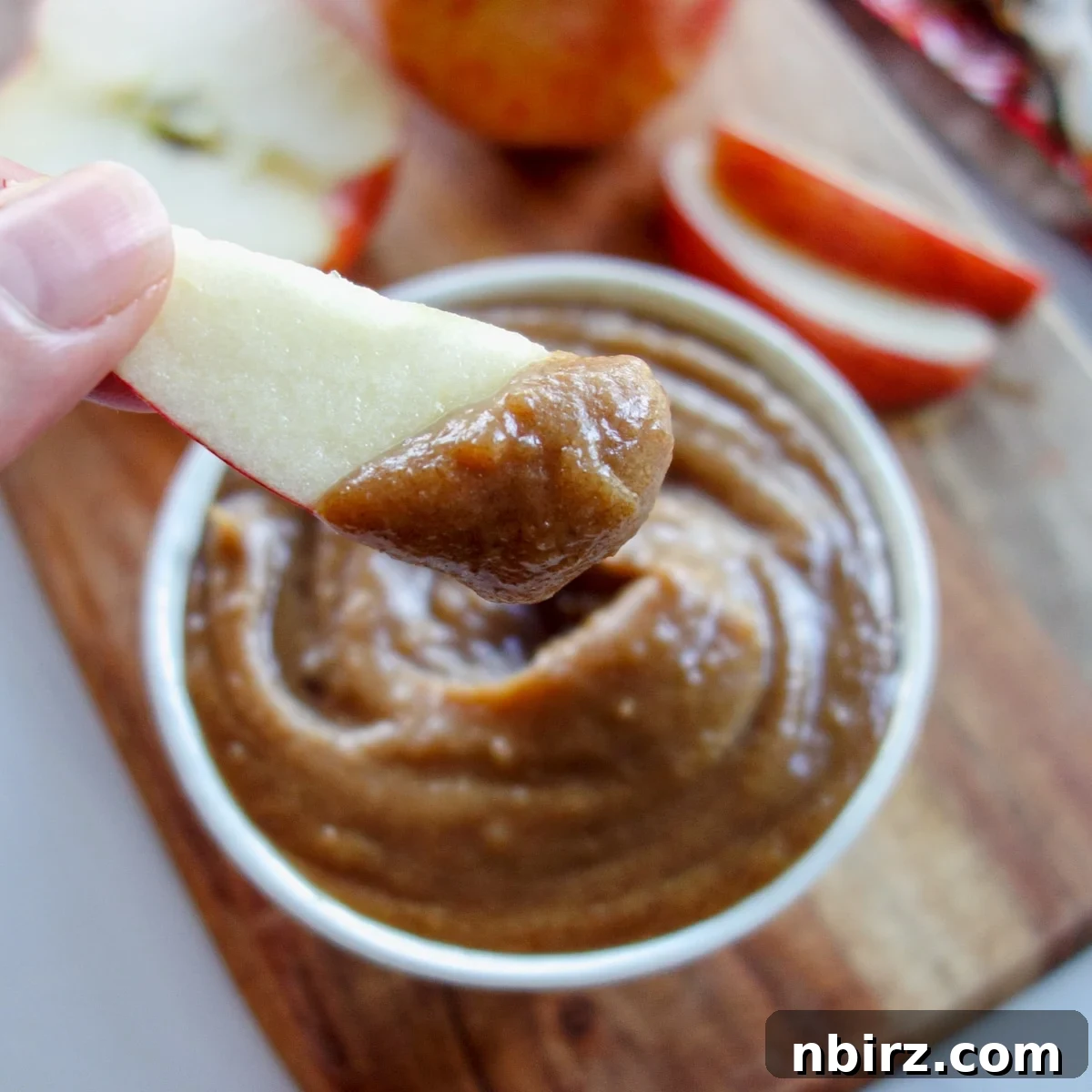 Creamy Date Caramel Dip with Apple Slices White bowl full of creamy date caramel dip, with a fresh apple slice perfectly dipped into it.