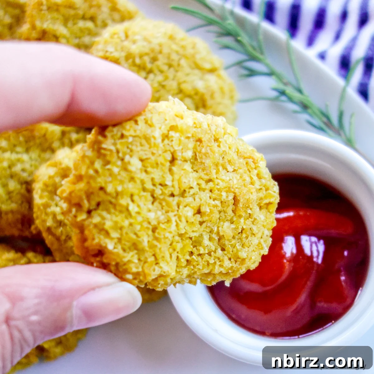 Protein-Packed Millet Nuggets: Just Two Ingredients 9 A close-up of a crispy millet nugget about to be dipped into a vibrant red ketchup