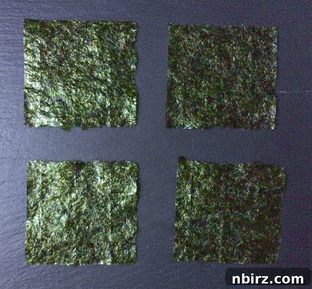 Effortless Plant-Based Gluten-Free Sushi Cups 4 Four perfectly cut squares of nori (seaweed paper) neatly arranged on a piece of dark slate, ready for use.