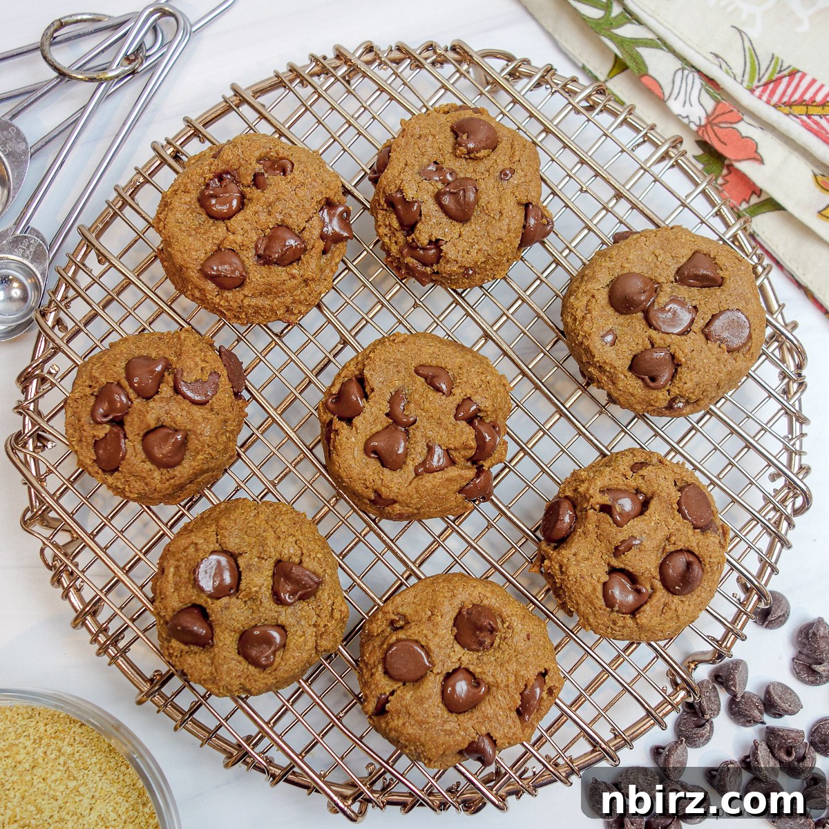 An overhead shot captures a collection of freshly baked chocolate chip flax cookies arranged on a copper cooling rack, highlighting their perfect round shapes and golden-brown hue.