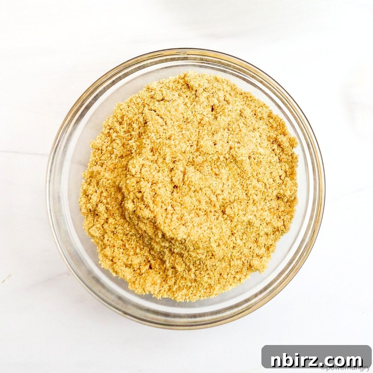 A glass bowl filled with finely ground golden flaxseed meal, ready for baking.