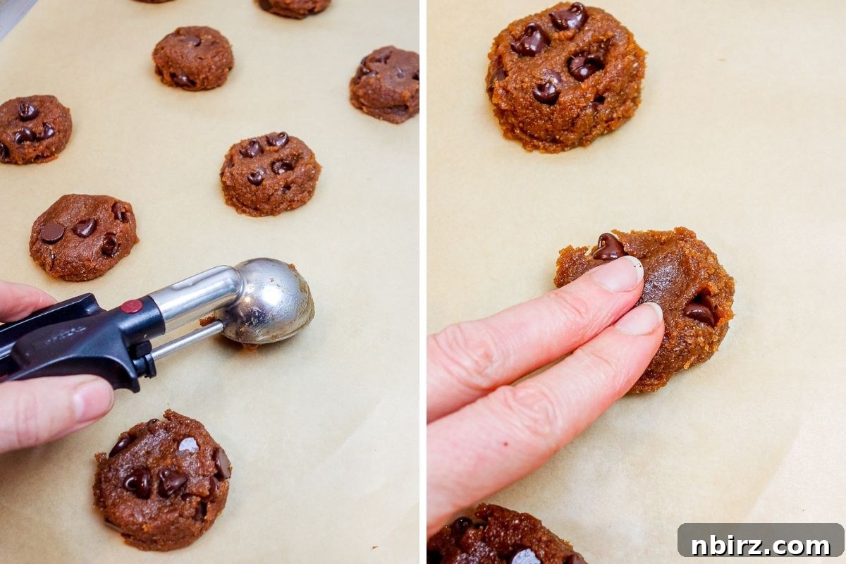 Portioned rounds of chocolate chip flax cookie dough flattened on a parchment paper-lined baking sheet, ready for the oven.
