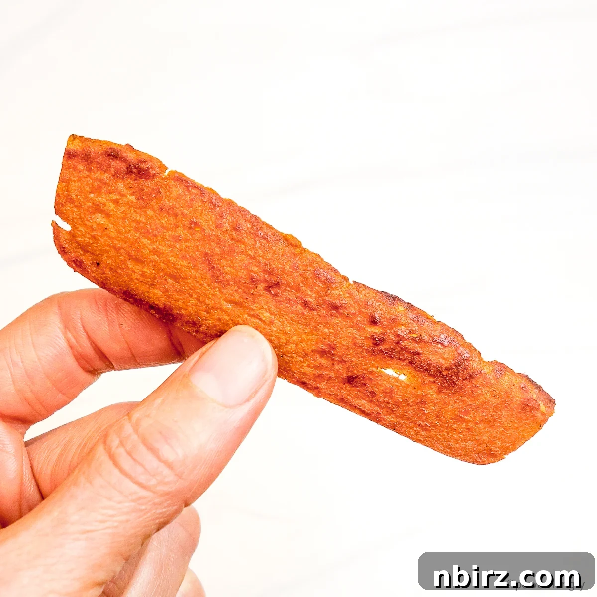Crispy Soy-Free Lentil Bacon 5 A single, perfectly cooked strip of lentil bacon held delicately in a hand, showcasing its texture.