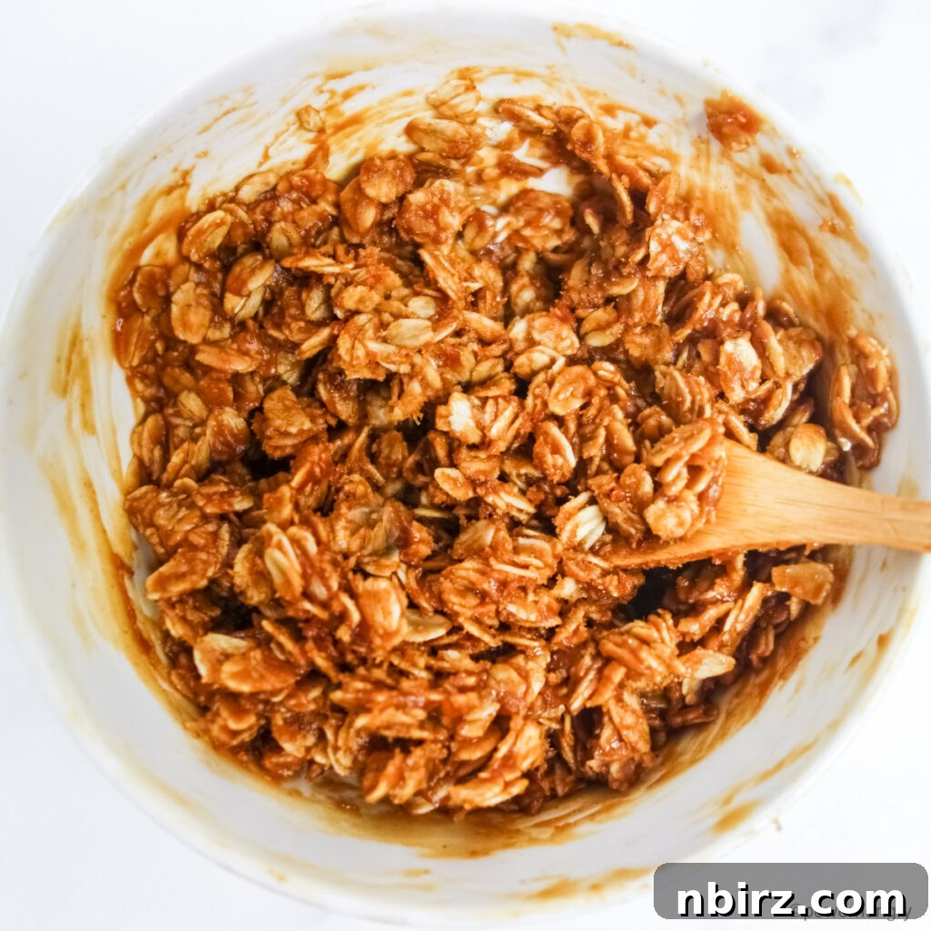 No-bake granola mixture in a white bowl with a wood spoon