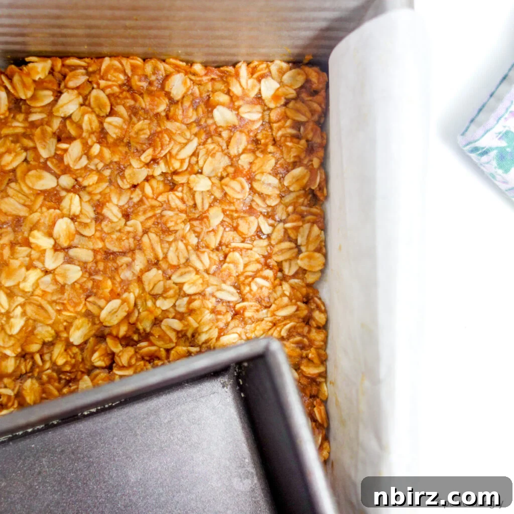 Granola bar mixture being pressed into a parchment paper-lined baking pan