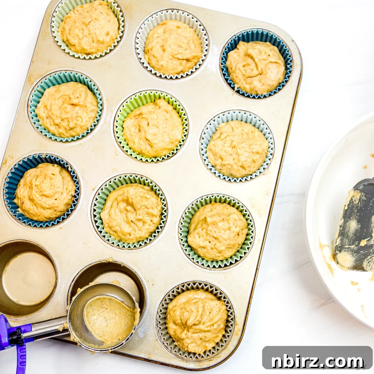 Wholesome Four Ingredient Banana Cassava Muffins 7 muffin batter being spooned into a muffin tin lined with silicone cups