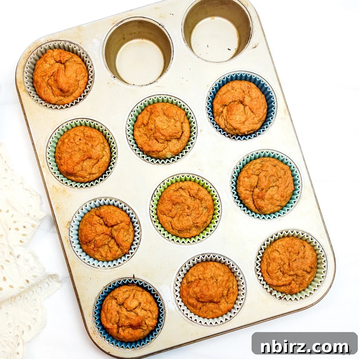 Wholesome Four Ingredient Banana Cassava Muffins 8 a silver muffin tin filled with freshly baked, golden-brown vegan muffins