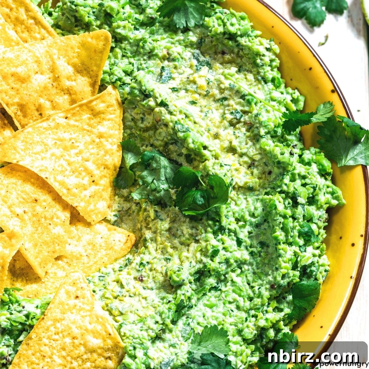 Green Pea Guacamole: No Avocado, No Problem 2 Freshly made green pea guacamole in a rustic serving bowl, garnished with a sprig of cilantro, ready for dipping.