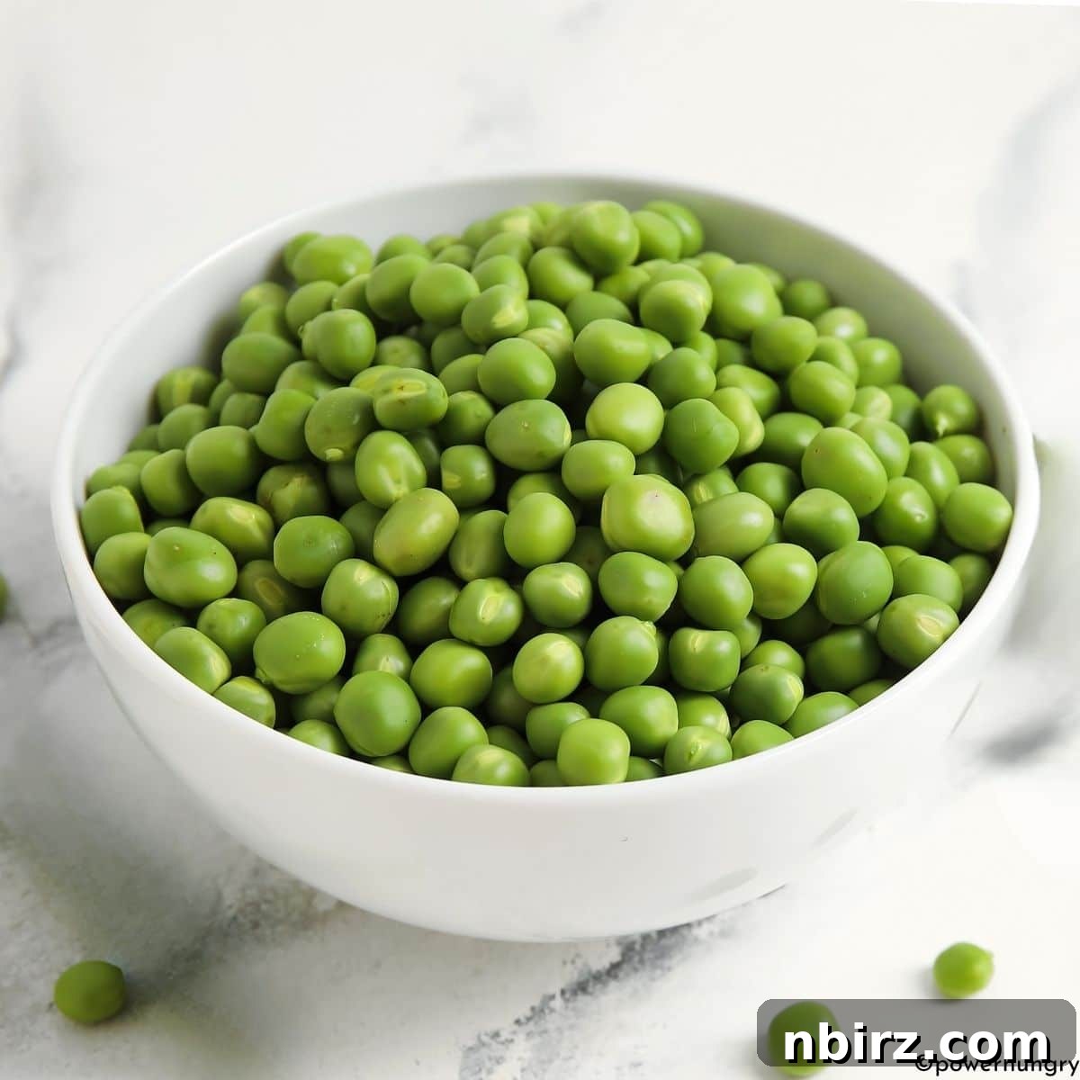 Green Pea Guacamole: No Avocado, No Problem 3 Close-up of vibrant green peas filling a pristine white ceramic bowl, emphasizing their natural freshness and health benefits.