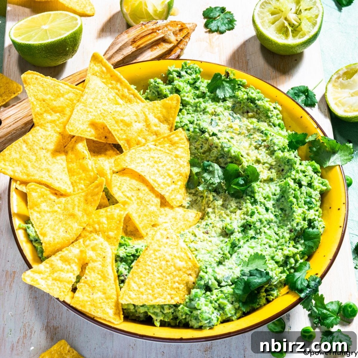 Green Pea Guacamole: No Avocado, No Problem 4 A bowl of vibrant green pea guacamole with a spoon nestled inside, ready to be enjoyed, showing a perfectly textured dip.