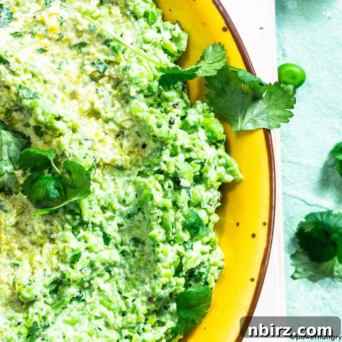 Green Pea Guacamole: No Avocado, No Problem 5 A close-up shot of green pea guacamole, highlighting its creamy yet textured consistency, with fresh cilantro scattered on top for garnish.