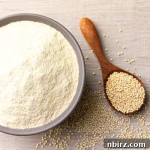 Quinoa flour in a bowl with a wooden spoon and whole quinoa seeds beside it