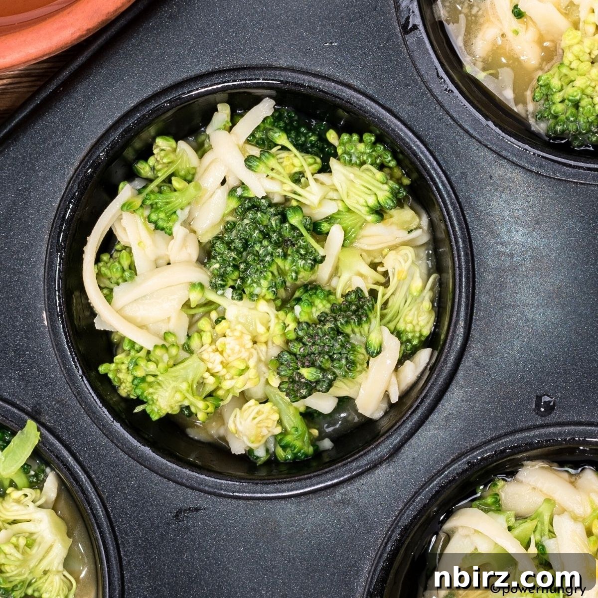 Muffin tin with broccoli and chopped onion already divided into the cups, before the chickpea flour batter is added.
