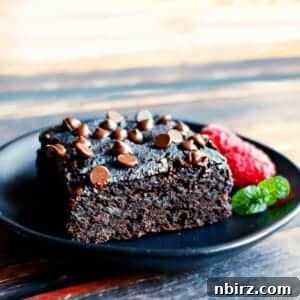 vegan breakfast brownie on a black plate, with raspberries and a mint sprig alongside