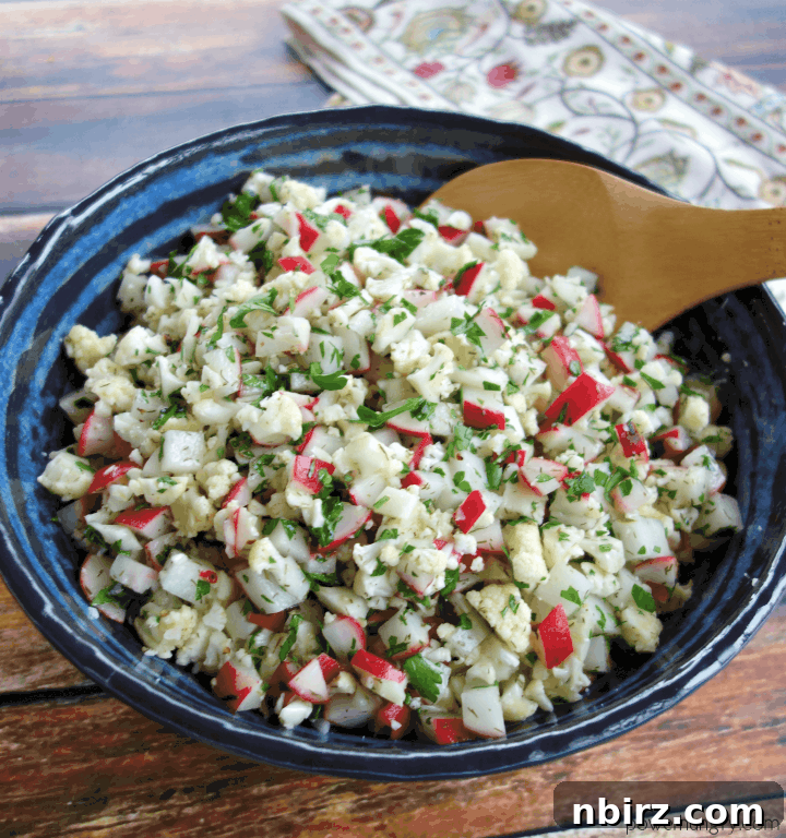 Close-up of chopped radish cauliflower salad in a blue and black pottery bowl with a wooden spoon, showcasing its fresh texture