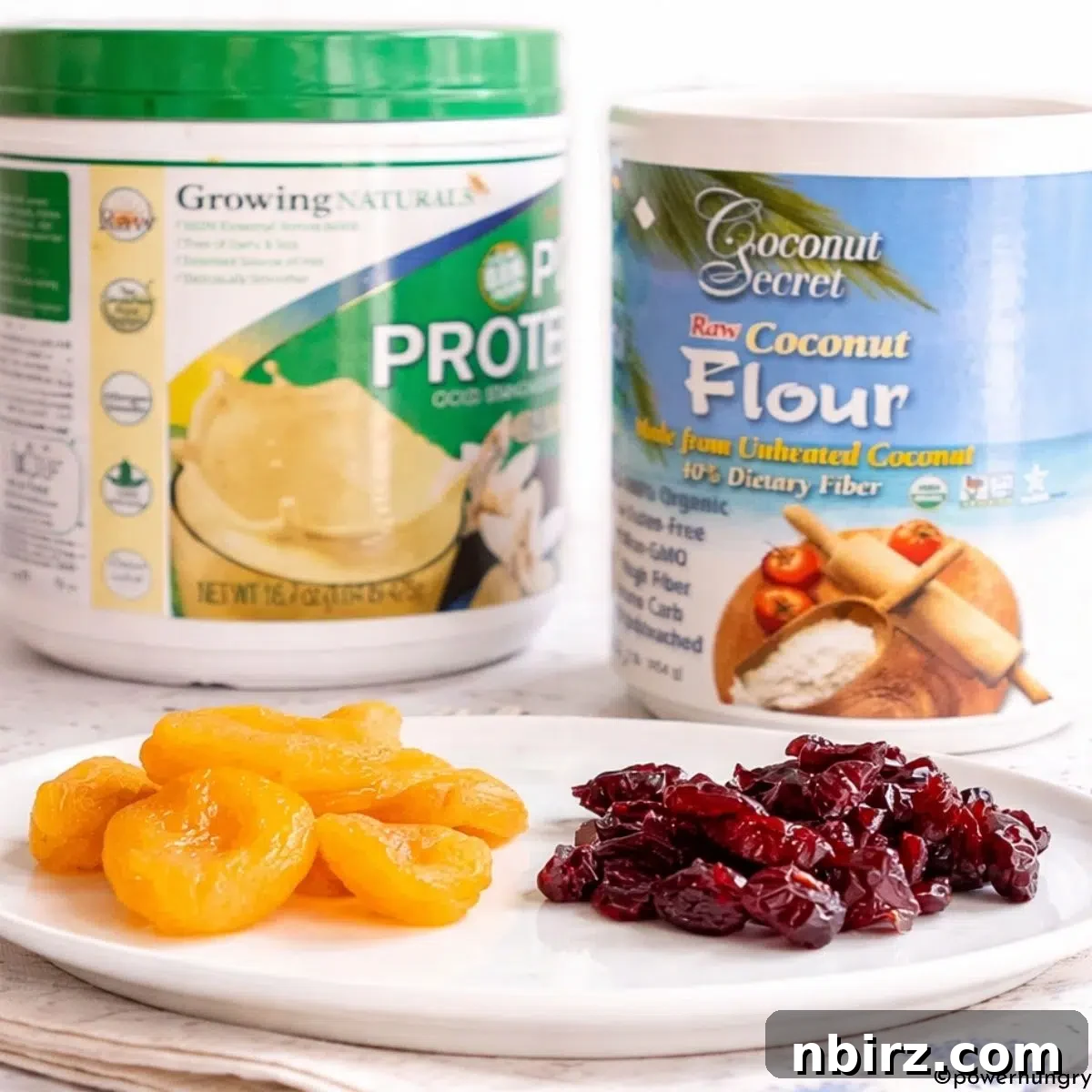 Three main ingredients for the protein bars: a bowl of dried fruit, a scoop of vanilla protein powder, and a small container of coconut flour.