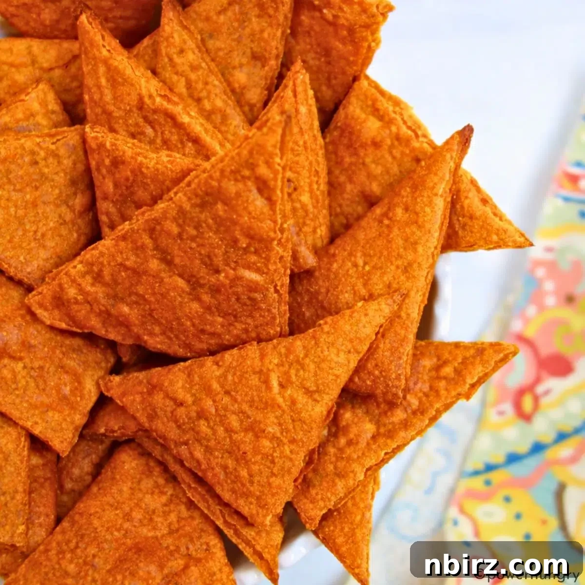 Crunchy Zesty High Protein Lentil Chips Vegan Grain Free 2 Close-up of vibrant high-protein nacho cheese lentil chips in a white bowl, showcasing their crispy texture and rich orange color.