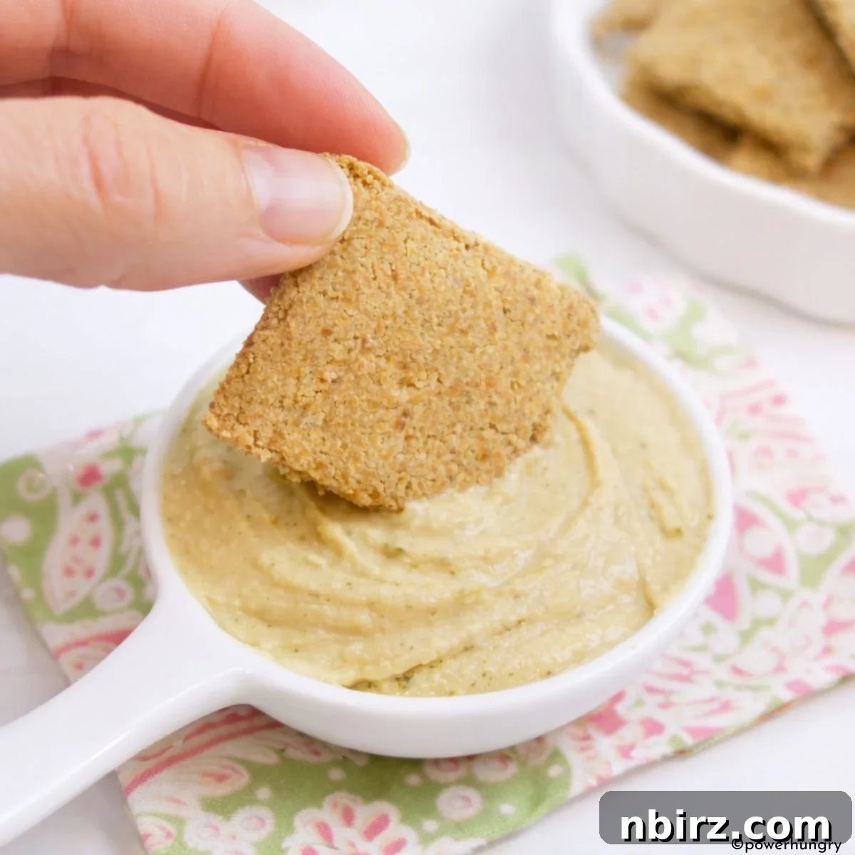 Another shot of 2-Ingredient Chickpea Flour Crackers being dipped into creamy hummus, emphasizing their versatility for entertaining or snacking