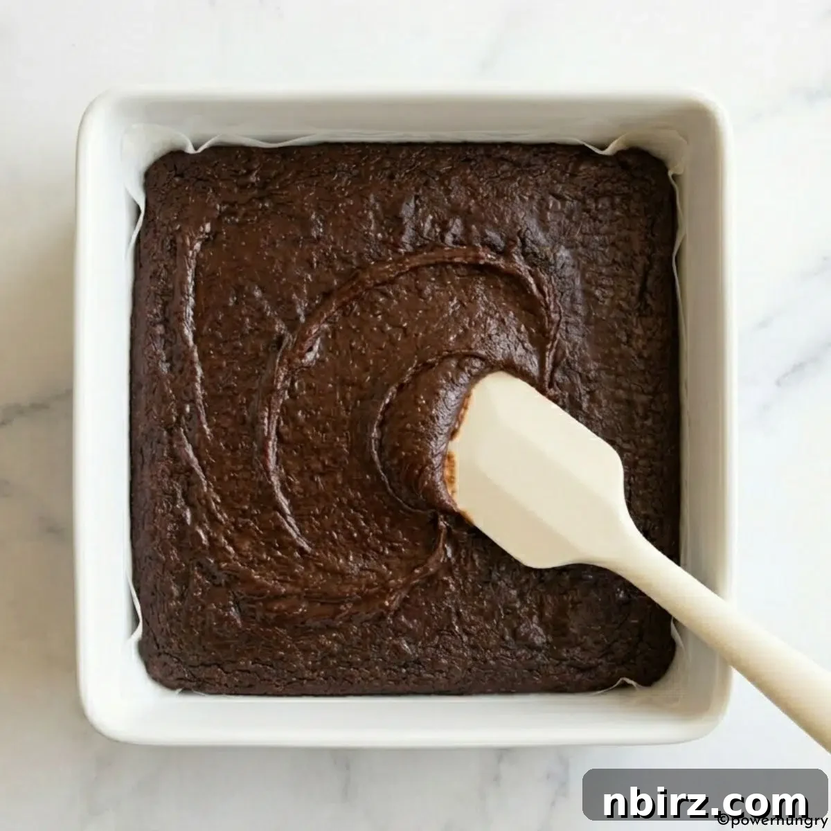 Decadent Grain-Free Vegan Carob Almond Brownies 7 Thick carob brownie batter being spread smoothly into a parchment-lined square baking pan.