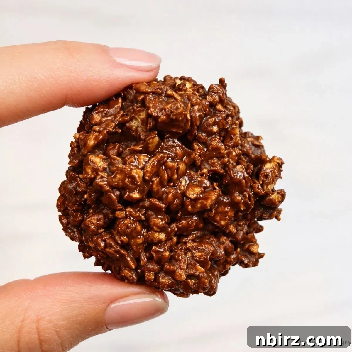 a single 3 ingredient chocolate no-bake protein cookie, held in fingertips