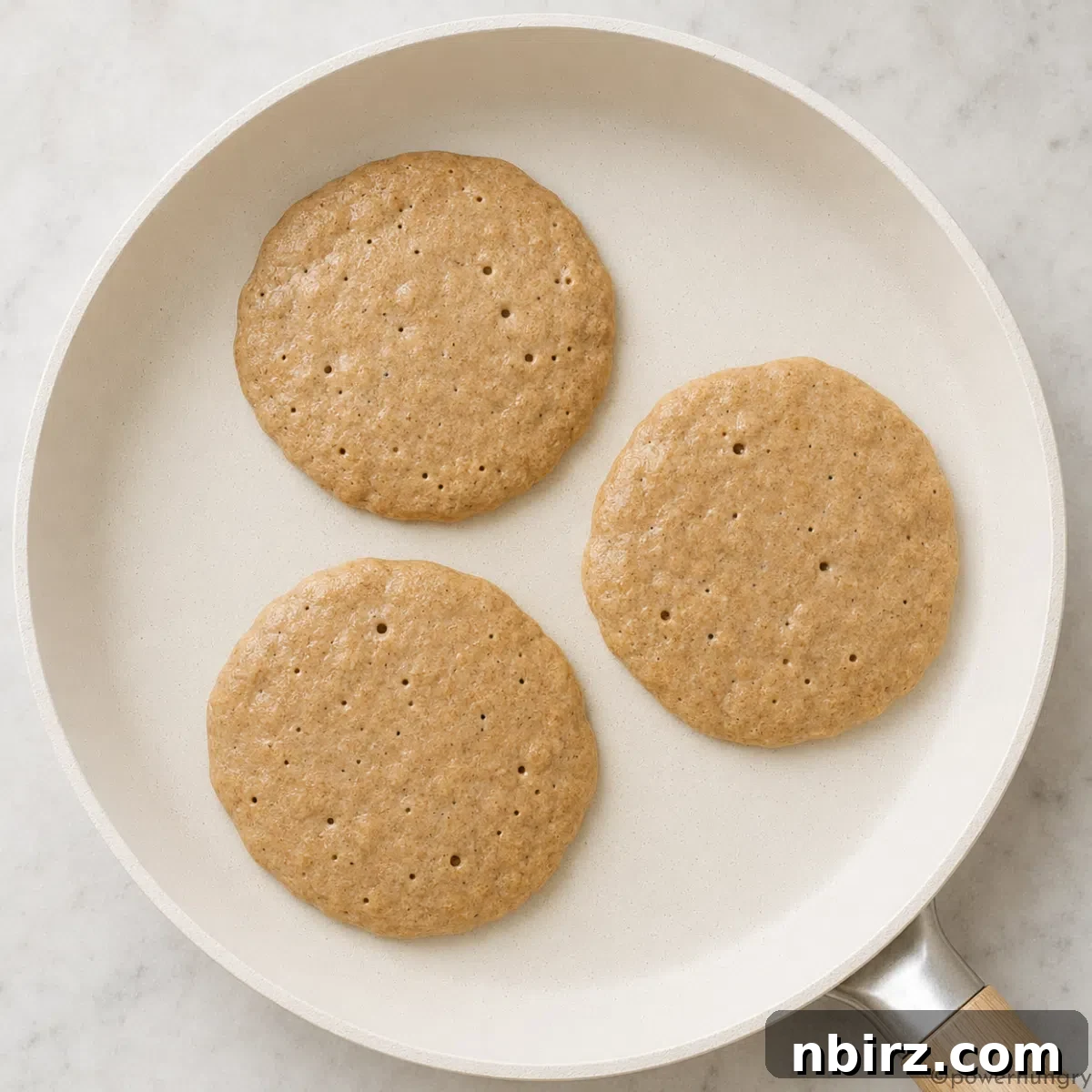 Fluffy Gluten-Free Vegan Buckwheat Pancakes 5 nonstick ceramic skillet with three buckwheat pancakes that are cooking